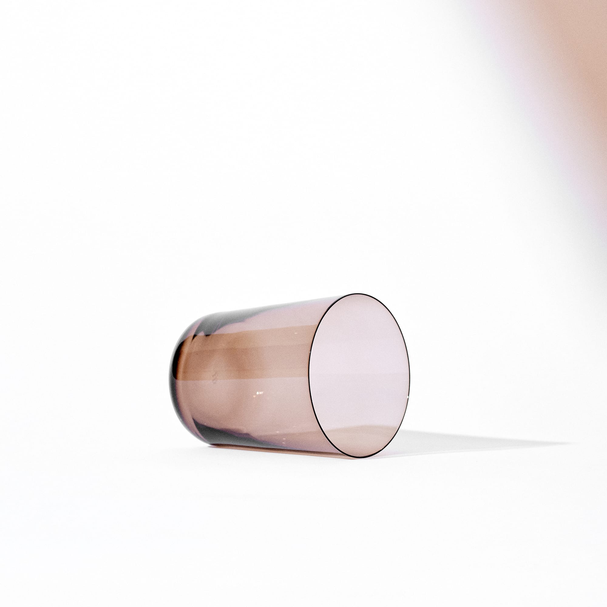 Minimalist Scandinavian clear brown glass tumbler laying on its side with soft shadow on white background