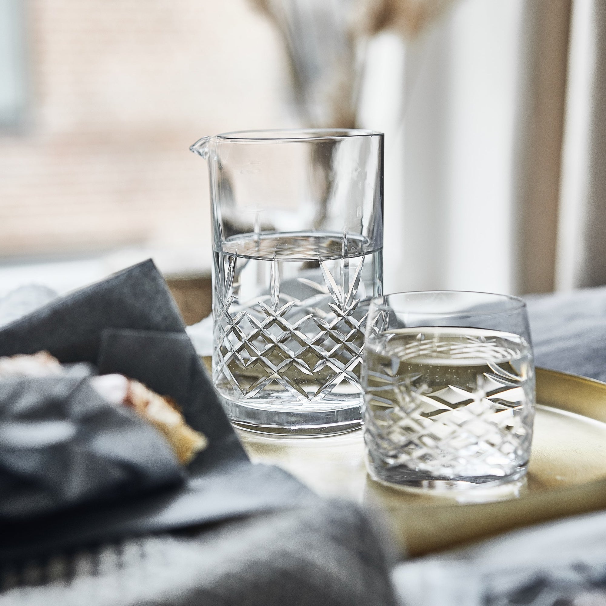 Clear crystal glass pitcher and matching glass with diamond pattern on a brass tray in a Scandinavian home setting